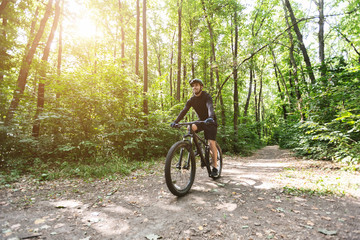 Naklejka premium Male cyclist riding on forest trails in sun flare