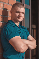 Young handsome sporty man with biceps in a blue shirt against a brick wall.