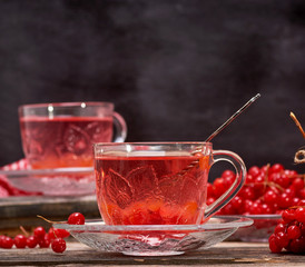viburnum tea in a transparent cup with a handle and saucer on a gray wooden table
