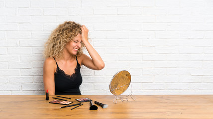 Young woman with lots of makeup brush in a table having doubts with confuse face expression