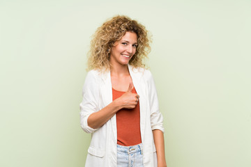 Young blonde woman with curly hair over isolated green background giving a thumbs up gesture