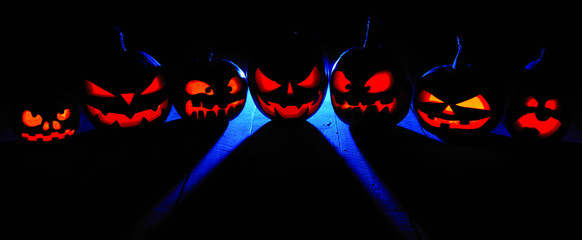 The concept of Halloween. Many glowing fiery light angry scary pumpkins. jack lantern in the dark, with a blue cool light behind on a wooden background