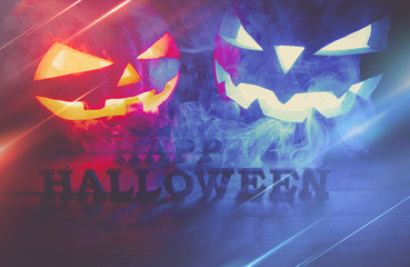 The concept of Halloween. two glowing oranjous and blue light angry scary pumpkin with smoke, jack-lantern, with an inscription of a happy Halloween, on a wooden background