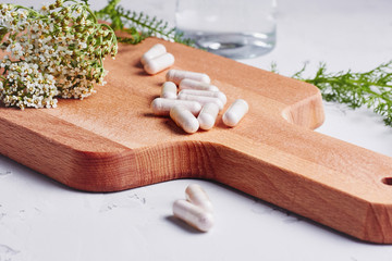 Alternative medicine, naturopath and dietary supplement. Herbal remedy in capsules and plants over grey background