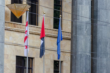 The flag of Georgia and the flag of the European Union on the background of a gray building, between them another flag