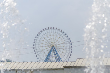 Ferris wheel with colored cabins in the amusement Park with a stream from the fountain on the sides in Sunny weather, Tbilisi