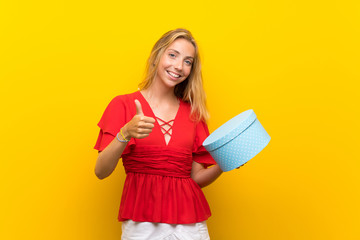 Blonde young woman over isolated yellow background holding gift box
