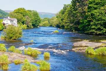 The clear waters of the River Dee flow quickly between its densely wooded banks in Llangollen, Wales
