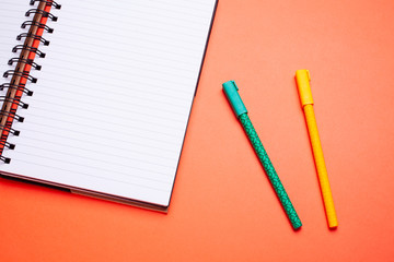 Flat lay top view mockup photo of working space with laptop and pens on orange pastel background.