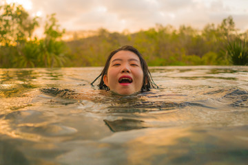 Fototapeta premium tropical holidays lifestyle portrait of young beautiful and happy Asian Korean woman in bikini enjoying sunset at amazing jungle resort infinity pool swimming relaxed
