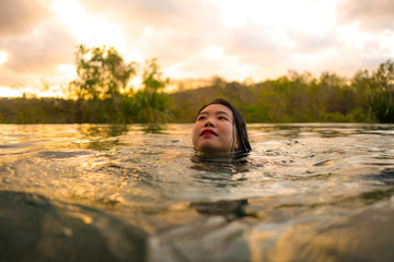 tropical holidays lifestyle portrait of young beautiful and happy Asian Chinese woman in bikini enjoying sunset at amazing jungle resort infinity pool swimming relaxed