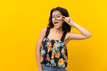 Young woman over isolated yellow background holding a magnifying glass