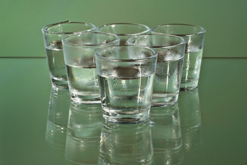 Alcoholic drink in clear glasses. Little cups isolated on green background. Frozen drinks on glass table.