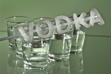Alcoholic drink in clear glasses. Little cups isolated on green background. Frozen drinks on glass table. The cups are stacked with a pyramid. Ice with the inscription - Vodka in the foreground.