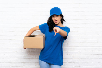 Young delivery woman over white brick wall surprised and pointing front