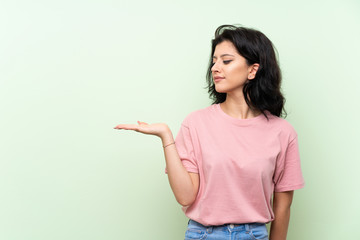 Young woman over isolated green background holding copyspace with doubts