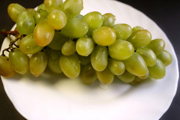 Bunch of green grape isolated on a plate on a black background