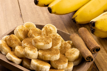 banana slices with cinnamon sprinkled and cinnamon sticks with bunch of bananas in the background