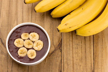 bunch of ripe bananas with açaí smoothie in bowl on wooden table top view