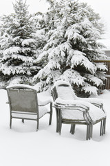 Snow-covered  fir-tree in the garden and stacked chairs of garden furniture.