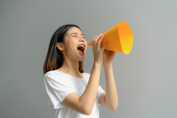 Attractive young Asian woman holding paper megaphone and yelling into.