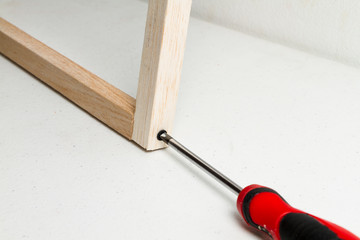 Destornillador rojo uniendo dos palos de madera de balso con tornillo negro sobre un fondo blanco