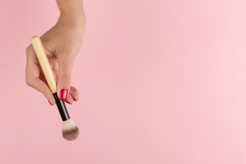 Girl's hand hold makeup brush on a pink background, copy space.