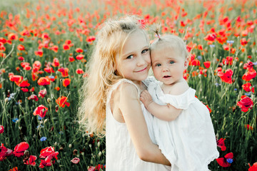 a girl holds her little sister on the poppy field