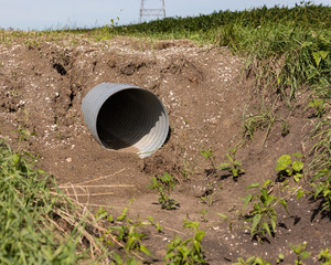 New corrugated metal drainage culvert pipe installed in ditch along road for access to farm field - obrazy, fototapety, plakaty
