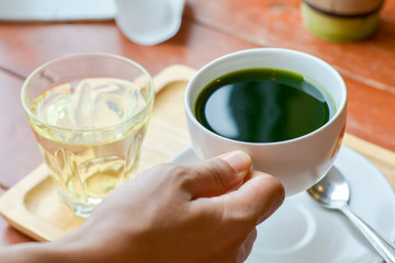 Hold hot matcha (green tea) in white ceramic cup on hand served on wooden tray on table in cafe and coffee shop. Healty beverages of japan for reduce sugar in blood.
