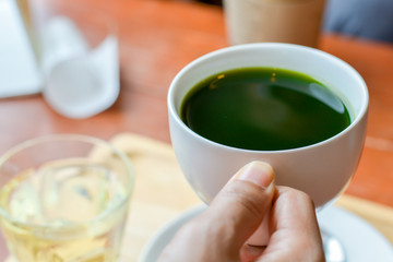 Hold hot matcha (green tea) in white ceramic cup on hand served on wooden tray on table in cafe and coffee shop. Healty beverages of japan for reduce sugar in blood.