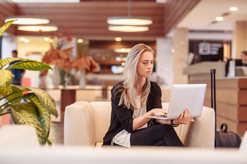 Positive smiling young beautiful caucasian business woman checks mail and works in the program using a laptop and high speed internet. Business Travel Concept