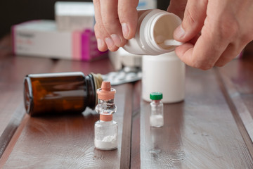 A man's hand holds a white pill and a bottle of pills. In the foreground are bottles of powders for medicinal solutions