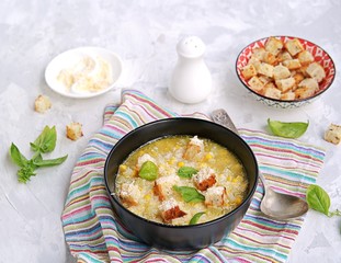 Summer soup of sweet corn and potatoes in a black bowl on a light gray concrete background. Served with croutons and grated parmesan cheese. Italian food. Selective focus.