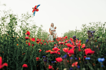 a mother with a baby and her elder daughter with a toy are among a flower field