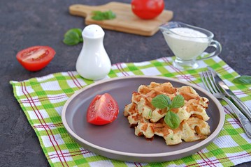 Savory zucchini waffles on a white plate on a dark concrete background. Served with ranch dressing and fresh tomato. Healthy food.
