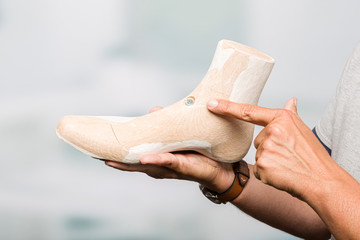 hands of a orthopedic shoemaker presenting an individual crafted wooden last