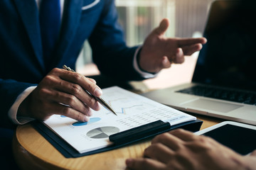 Two businessmen are discussing and analyzing the performance of the company business paper and...