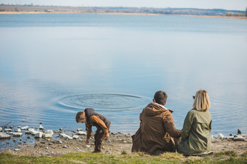 family walking near water. sitting at the beach. little kid throwing rock in water