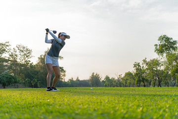 Healthy Sport. Asian Sporty woman golfer player doing golf swing tee off on the green evening time,...