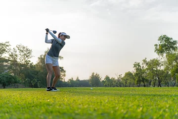 Deurstickers Healthy Sport. Asian Sporty woman golfer player doing golf swing tee off on the green evening time, she presumably does exercise. Healthy Lifestyle Concept. © freebird7977