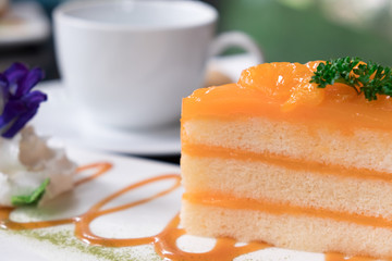 piece of layer orange cake on the plate at coffee shop in the morning. people eat cake and drink coffee for breakfast, lunch or coffee break at afternoon.