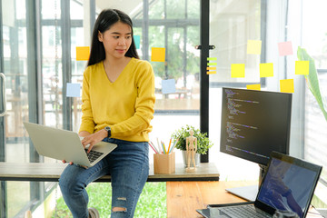 Asian female programmer for yellow shirt sit on the shelf and place laptop on leg.She stared at...