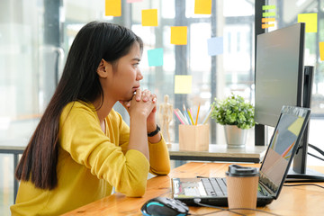 Obraz premium Asian female programmer for yellow shirt sitting with a hand on her chin,She stared at the computer screen and pondered.