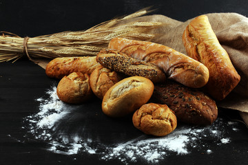 Assortment of baked bread and bread rolls on black table background