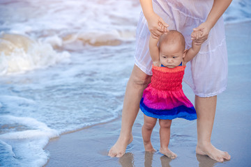 Ten months baby girl on the beach first time with mother. Infant feeling worry and excited playing on the beach. Mother hold daughter hands walking together.