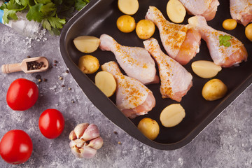Roasted chicken legs with potato, spices and herbs on the black pan.with vegetables on the background. Top view