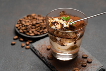 Portion of Classic tiramisu dessert in a glass cup on dark concrete background