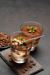 Portion of Classic tiramisu dessert in a glass cup on dark concrete background
