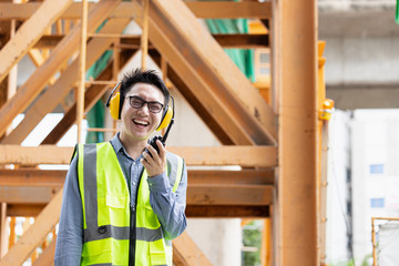 Image outside the industrial construction engineers in yellow protective ear muff discuss new project while using walkie talkie and happy smile on the open building site near the crane.